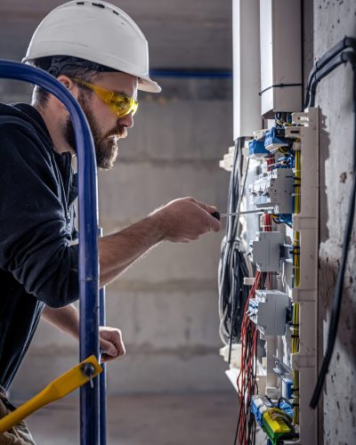 A male electrician works in a switchboard with an electrical connecting cable.